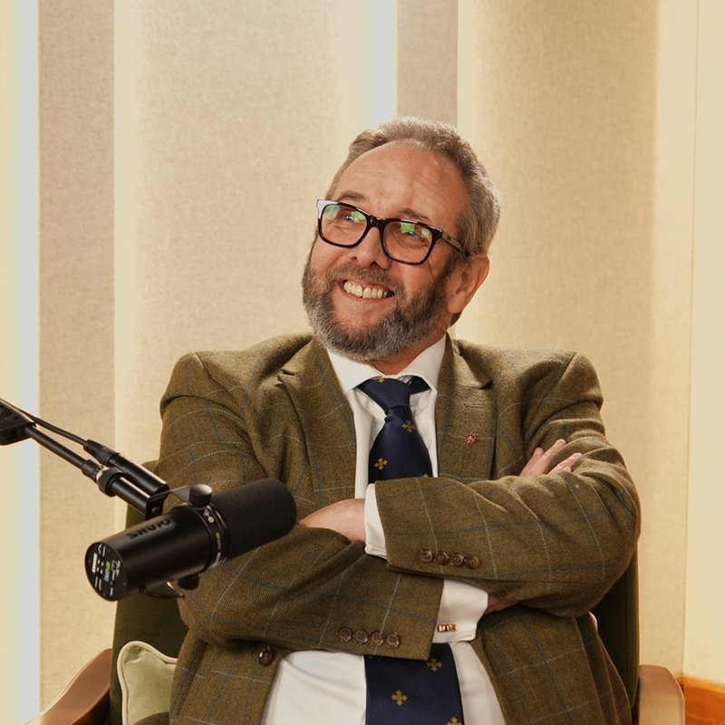 Al Kingsley laughing in a podcast studio, arms crossed beside a microphone