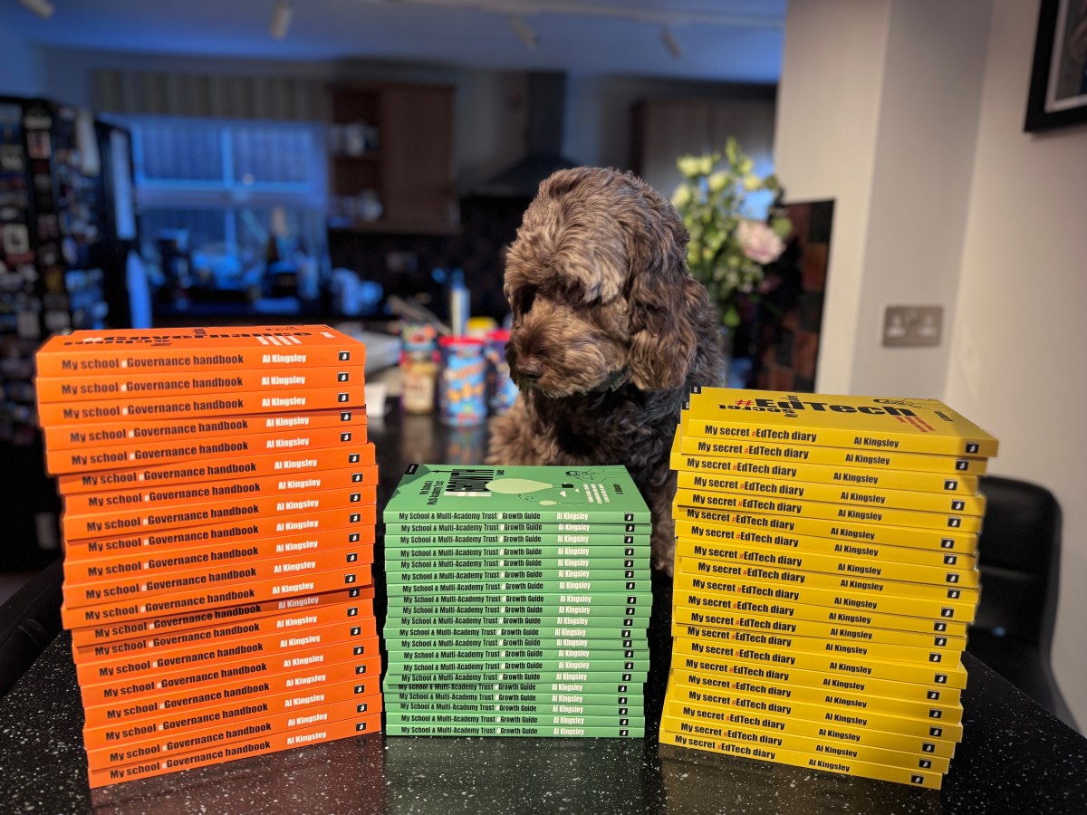 A cockapoo sitting beside two tall stacks of Al Kingsley’s books